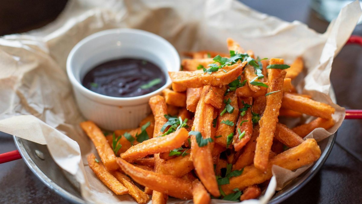 Close-up of crispy sweet potato fries garnished with parsley served with a dip.