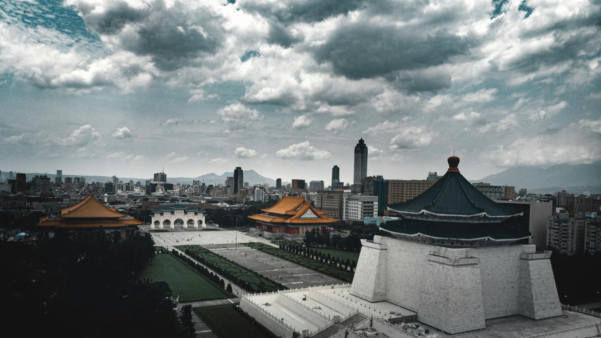 Historic stone temple with stairs surrounded by green lawn and contemporary multistage houses under sky with low clouds in overcast weather in evening in city