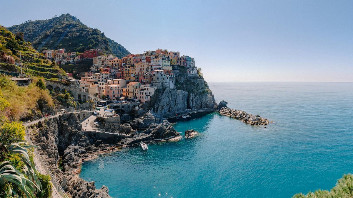 Breathtaking scenery of historic colorful buildings of famous coastal Manarola town located on stony hill in front of turquoise sea on sunny day