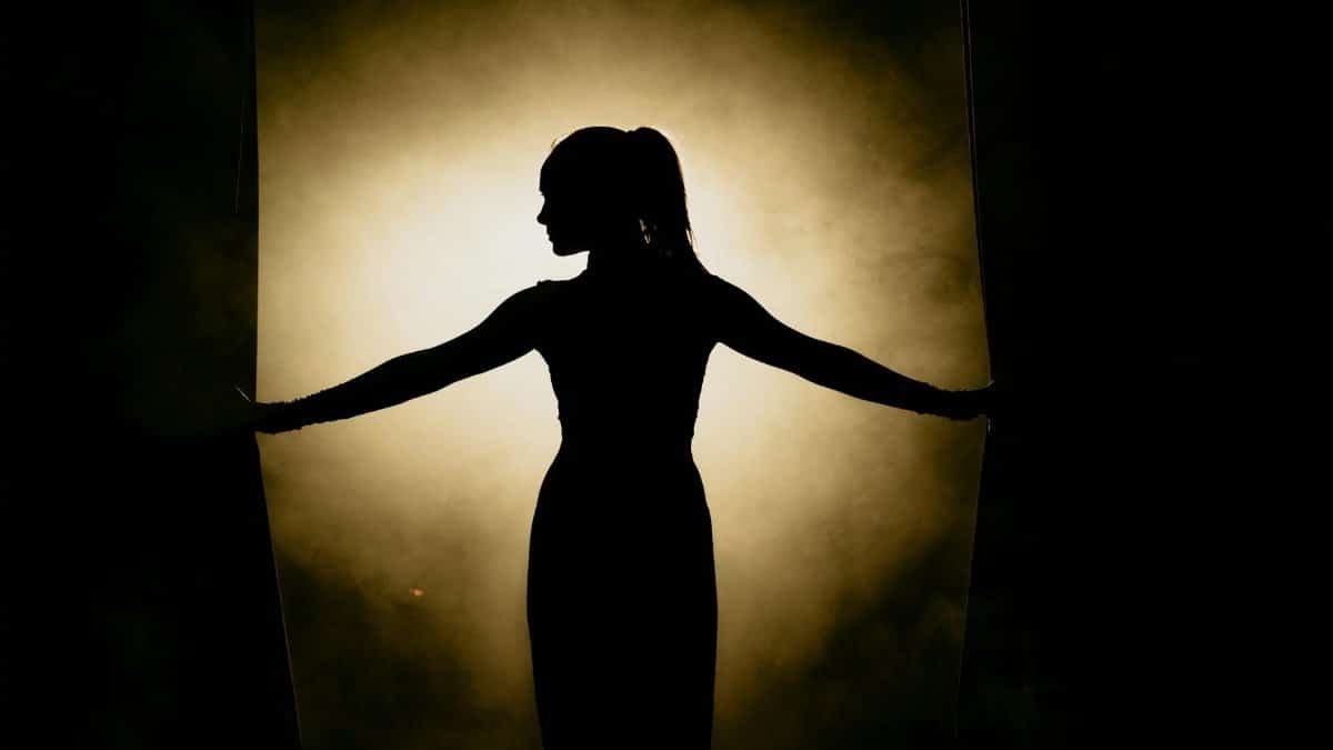 Artistic silhouette of a woman opening stage curtains, surrounded by smoke and spotlight.