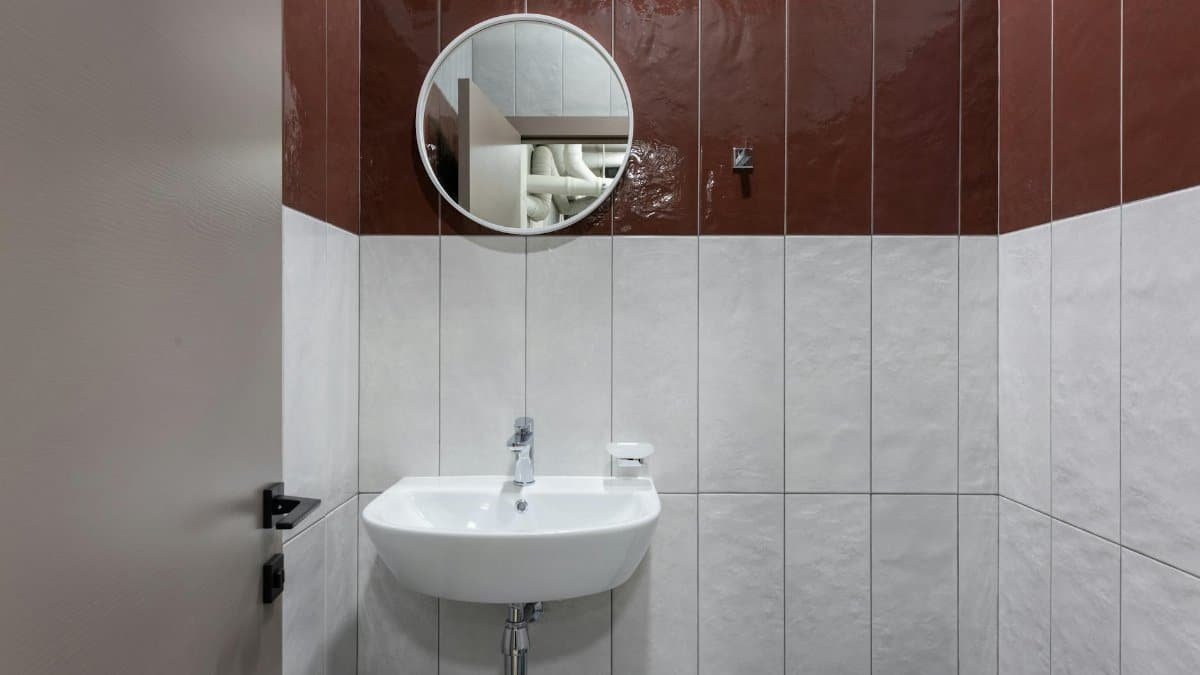 Modern interior of public bathroom with round shaped mirror above white ceramic washbasin and tiled walls