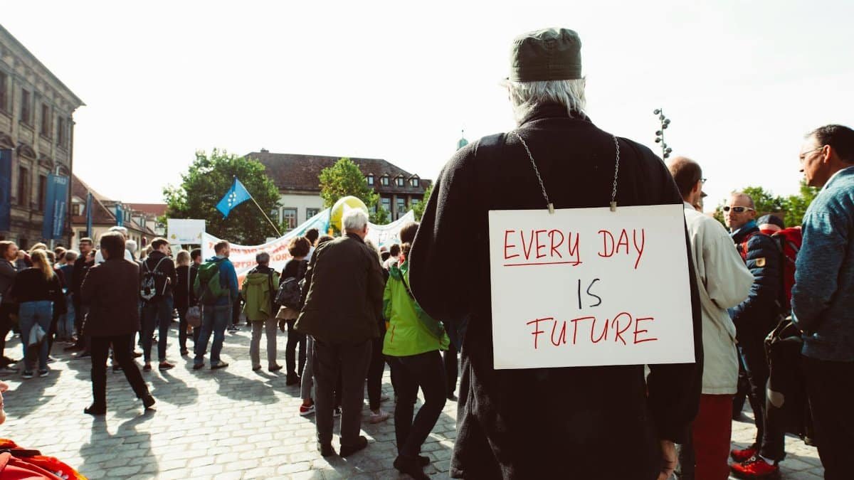 Participants at a climate rally gather on a cobblestone street with signs advocating for the future.