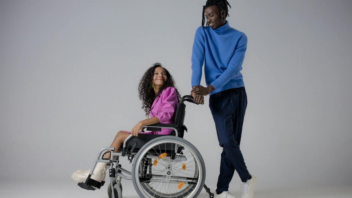 Charming couple smiling at each other in a studio setting with a wheelchair, portraying love and stylish fashion.