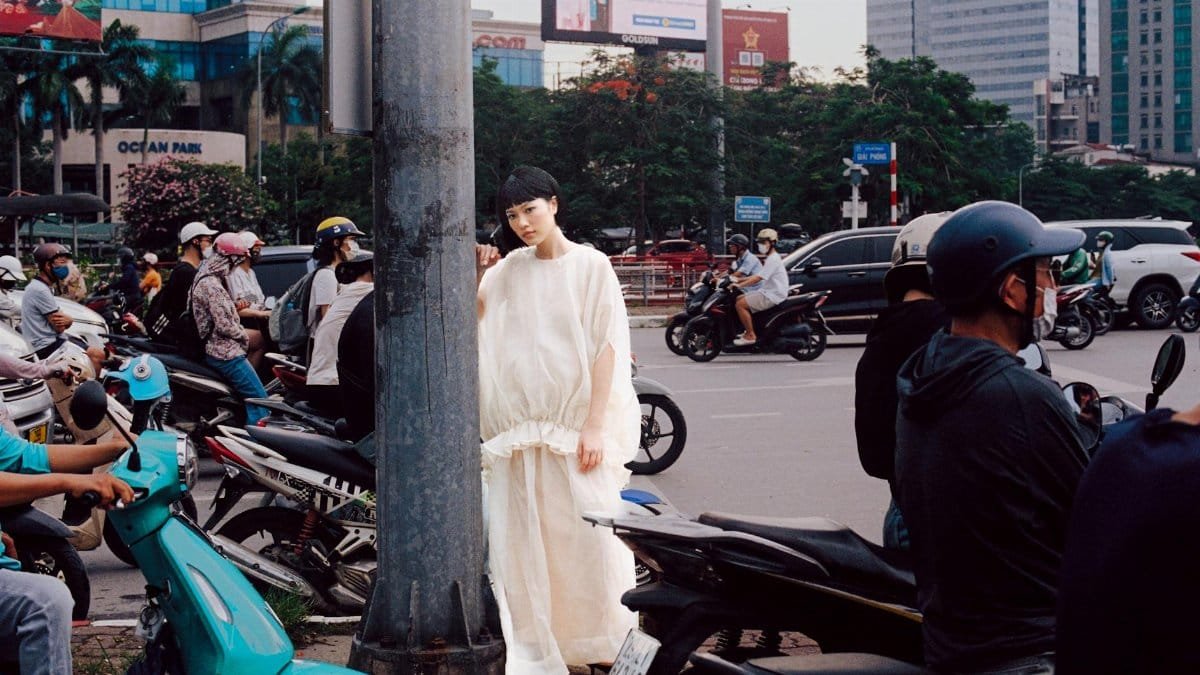 A model in a white dress poses amidst busy city traffic, creating a striking contrast.
