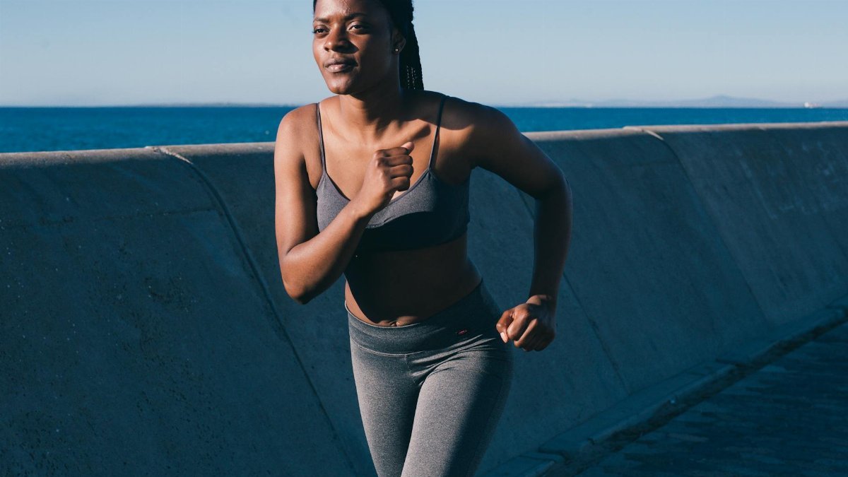 Healthy woman jogging along the oceanfront on a sunny day, embodying fitness and vitality.