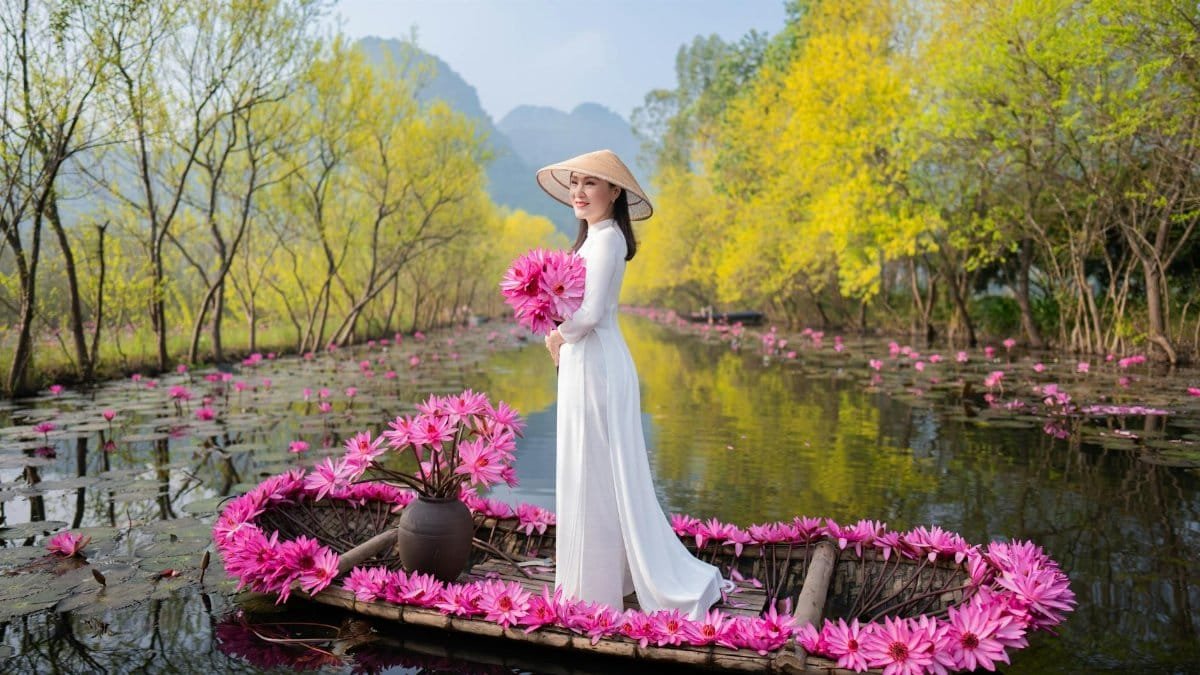 An elegant woman in a white dress on a flower-laden boat in a tranquil river setting, embodying traditional charm.
