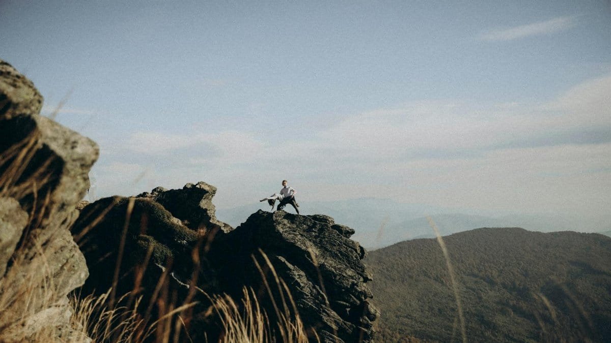 A couple gracefully dances on a rocky mountain peak under a clear sky, capturing a moment of freedom.