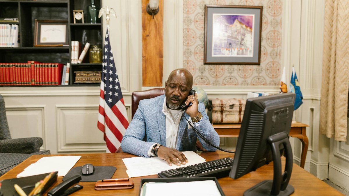 Businessman using phone in a classic office setting with an American flag and computer.