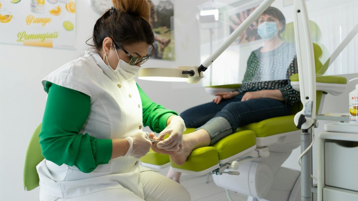 Concentrated professional master in beauty salon wearing medical mask doing pedicure during coronavirus epidemic