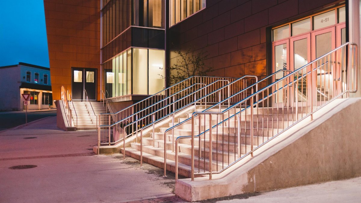 Contemporary building with illuminated entrance stairs at twilight, showcasing modern architectural design.