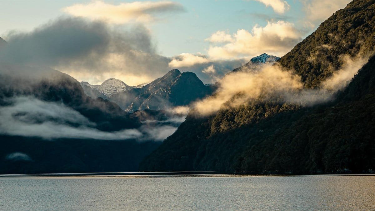 Breathtaking view of Lake Manapouri at sunrise with misty mountains, New Zealand.