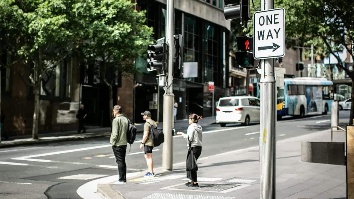 People waiting at a crosswalk on a sunny day in Alexandria, New South Wales with prominent one-way signage.