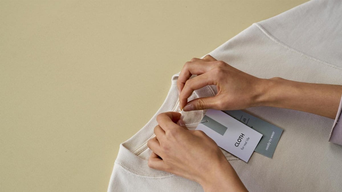 Hands removing a label from a white shirt on a neutral surface.