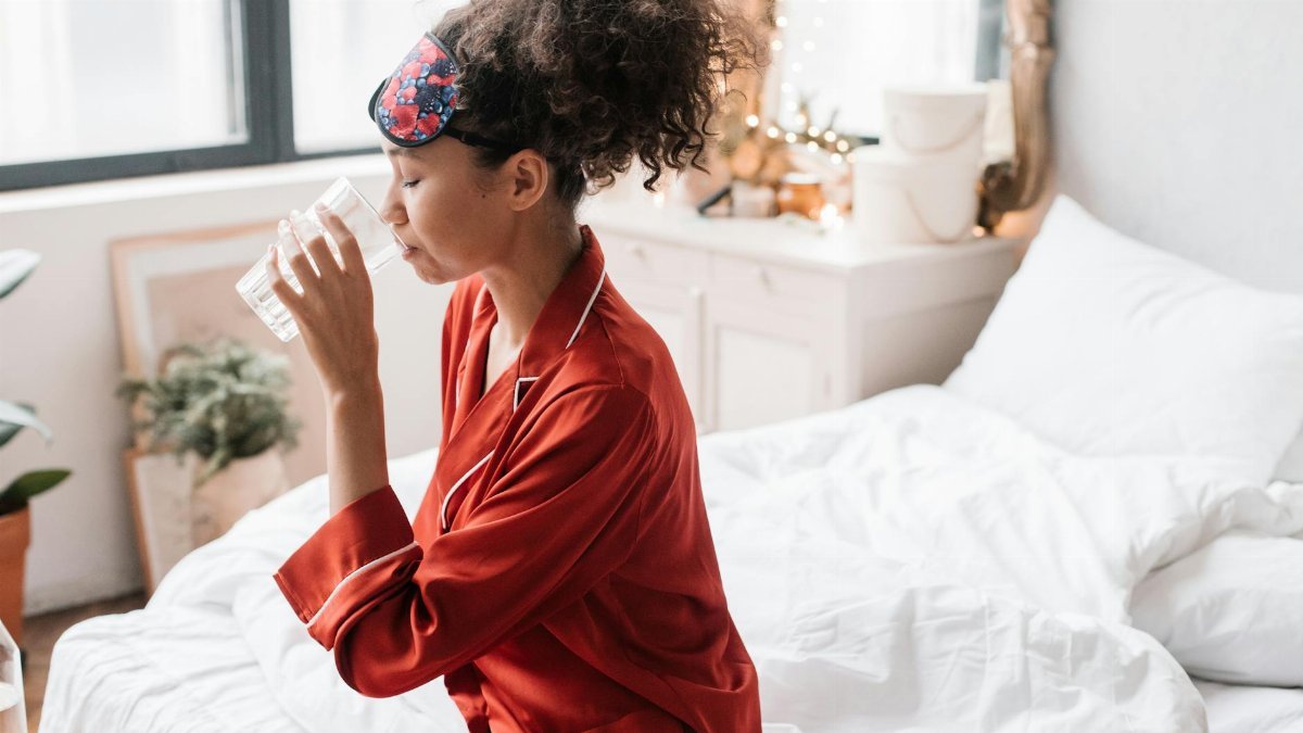 Woman in red pajamas drinking water, enhancing morning wellness rituals.