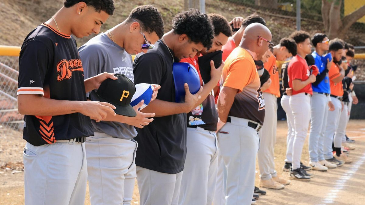 Baseball players lined up with caps off during a pre-game national anthem ceremony outdoors.
