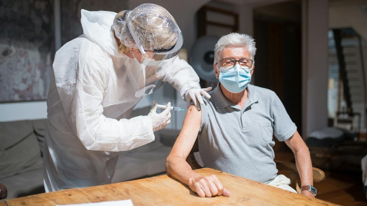 A healthcare worker administers a COVID-19 vaccine to an elderly man indoors, symbolizing health and safety.