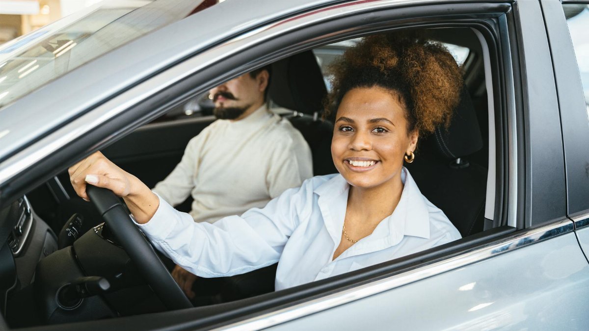 African American woman happily test driving a new car at a dealership. Capturing her joyful expression.