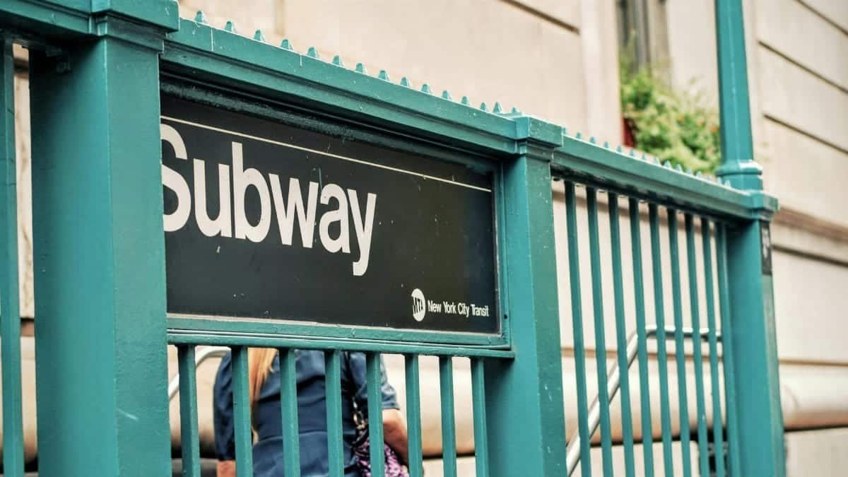 Close-up of New York City subway entrance featuring a green railing and people.