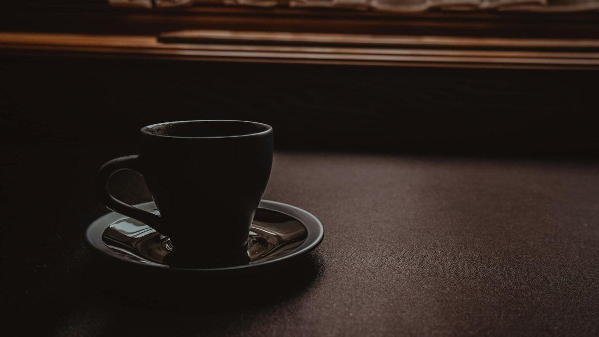 A minimalistic dark-toned image featuring a coffee cup on a table near a window.