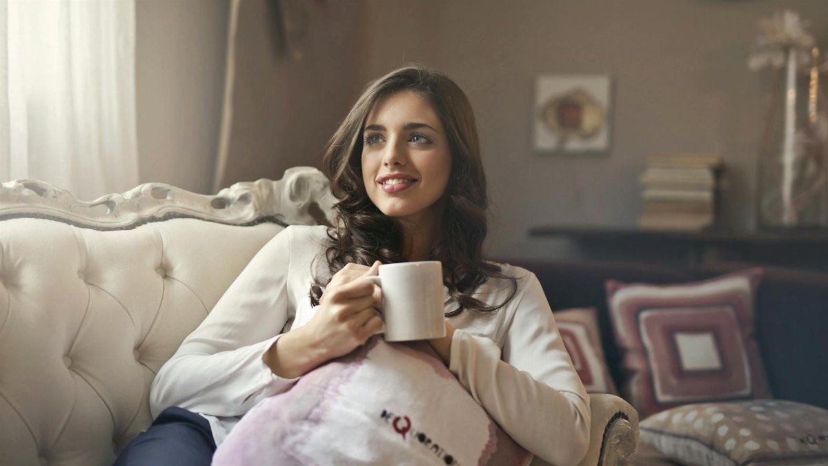 Woman relaxing with a cup of coffee on a sofa in a cozy living room.
