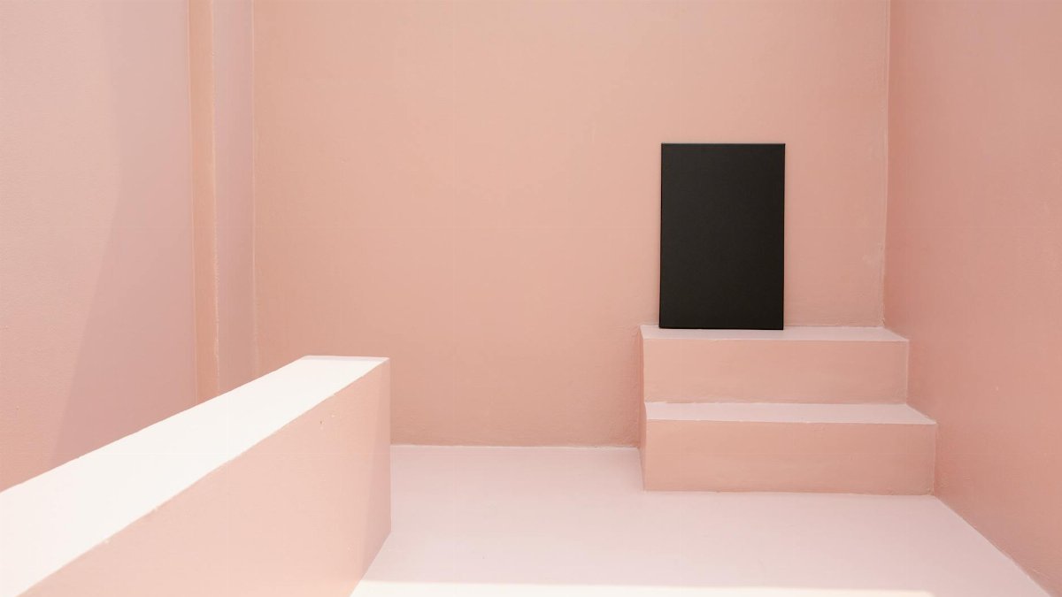 A modern minimalist pink room featuring a black canvas on small steps.