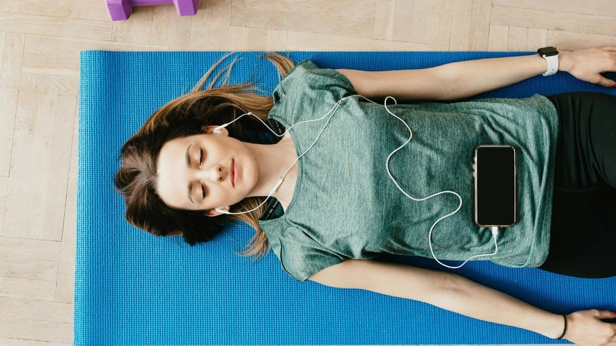 Young woman lying on a yoga mat listening to music for relaxation and mindfulness.
