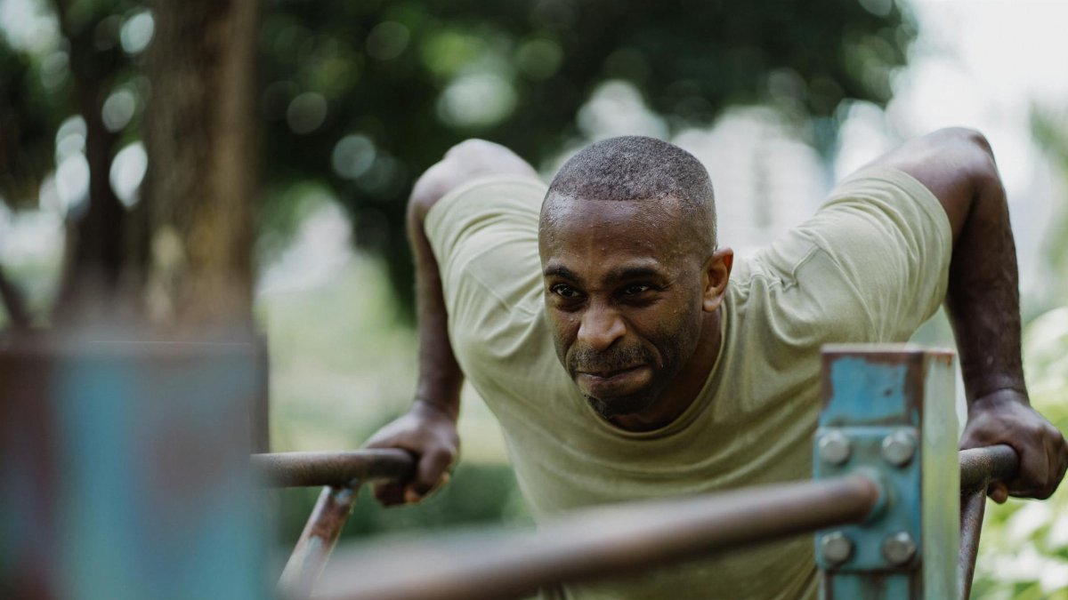 A determined man engaged in outdoor exercise dips on a sunny day.