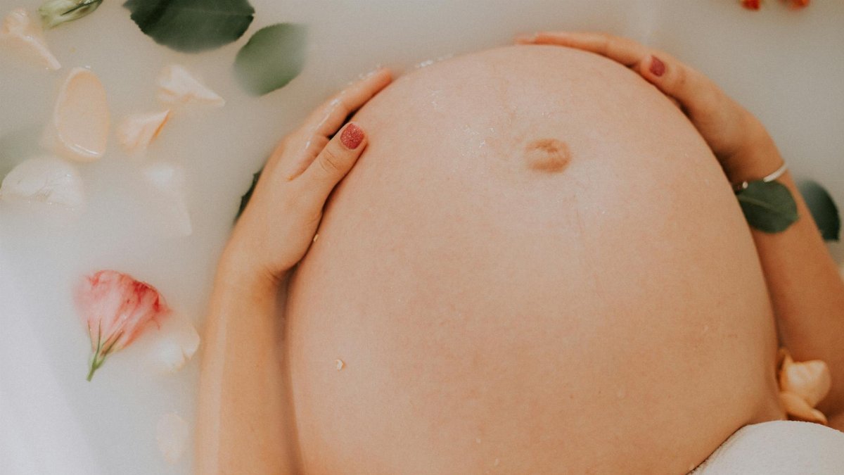 Pregnant woman relaxing in a soothing milk bath with flowers, embracing maternity.