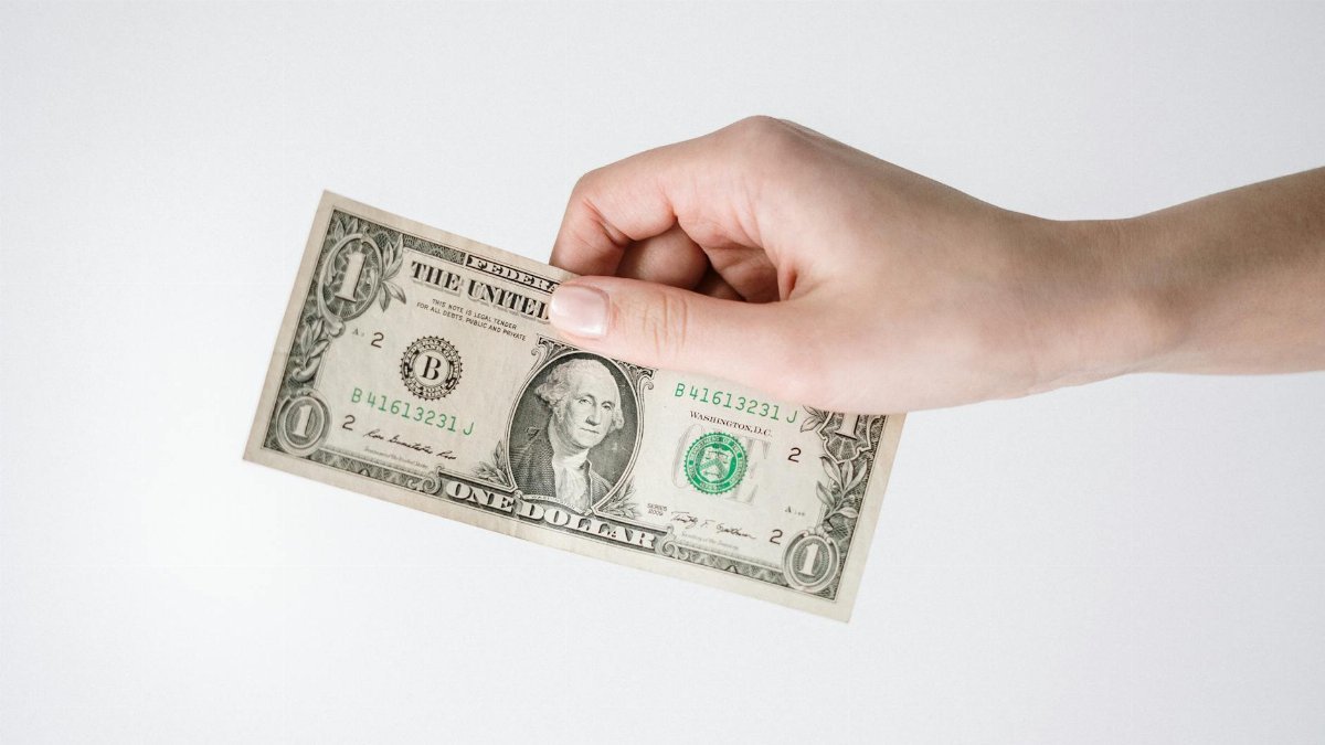 Close-up of a hand holding a one US dollar bill against a white background. Ideal for finance-related themes.