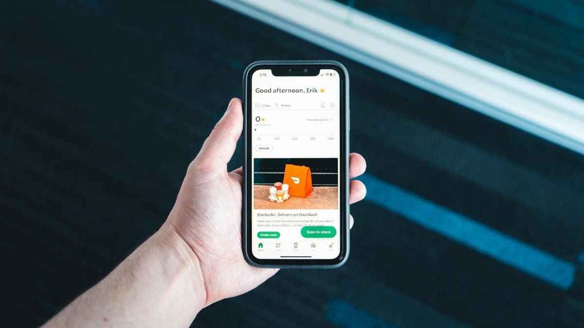 Hand holding smartphone with food delivery app on screen in bright setting.