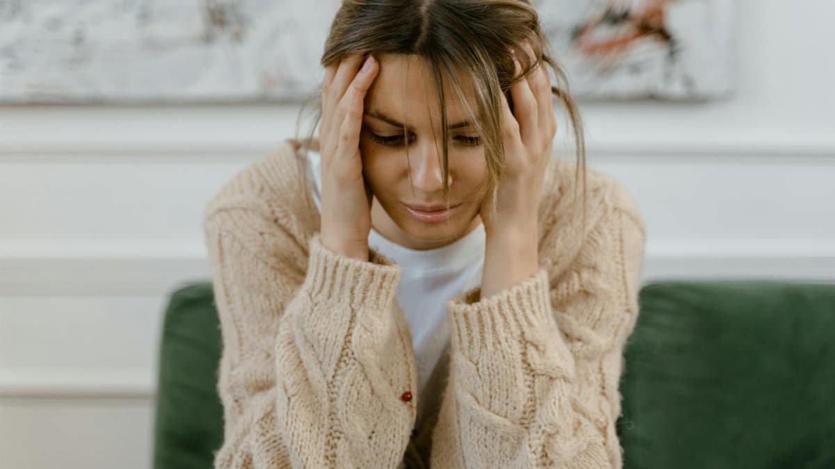 A woman sitting on a sofa holding her head, expressing stress and frustration indoors.