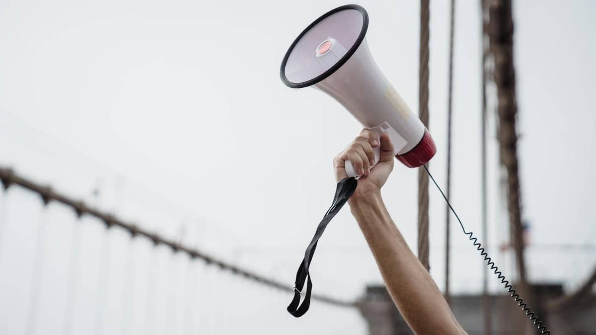 A hand holding a megaphone, symbolizing protest or announcement at an outdoor rally.