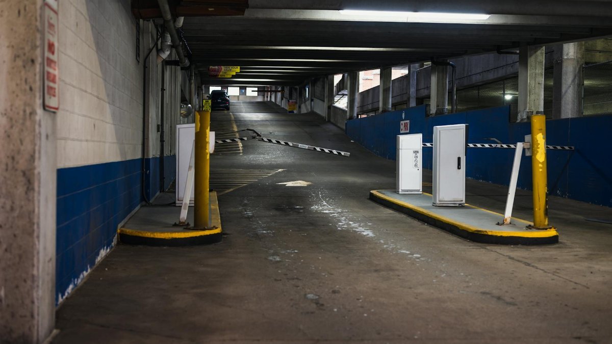 Entrance ramp of an underground parking garage with barriers and dim lighting, depicting urban infrastructure.