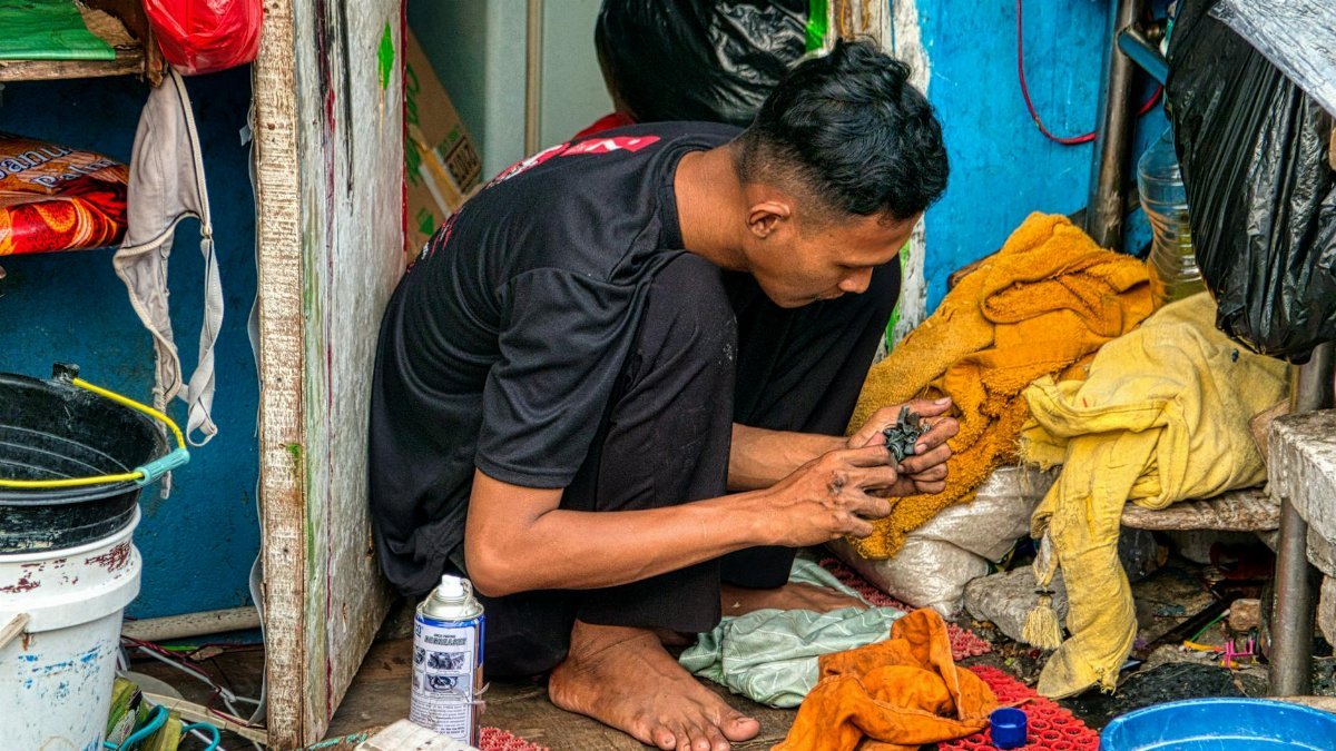 A young man focuses on his task amidst a modest setting in Jakarta, Indonesia.