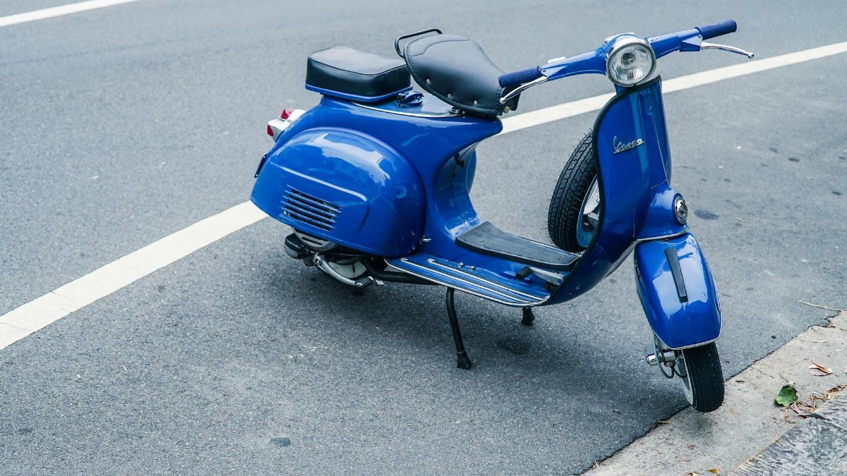 A classic blue Vespa scooter parked on a city street, showcasing retro style.