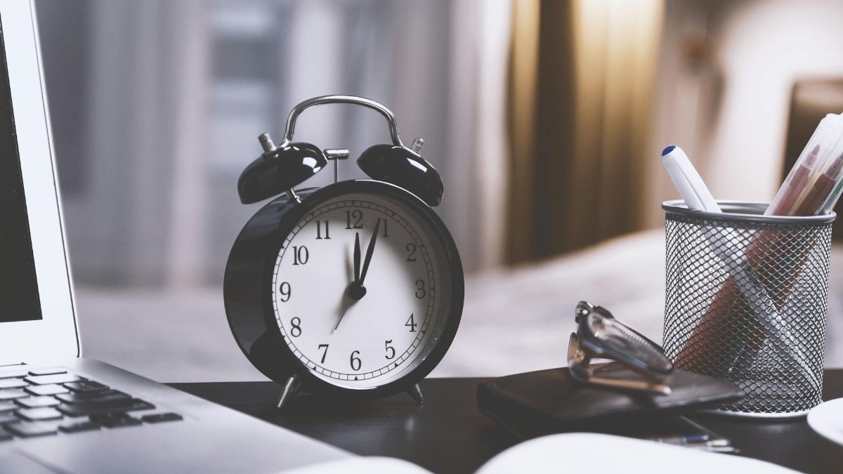 A classic analog alarm clock on a modern desk setup with a laptop and pens, creating a balanced workspace vibe.