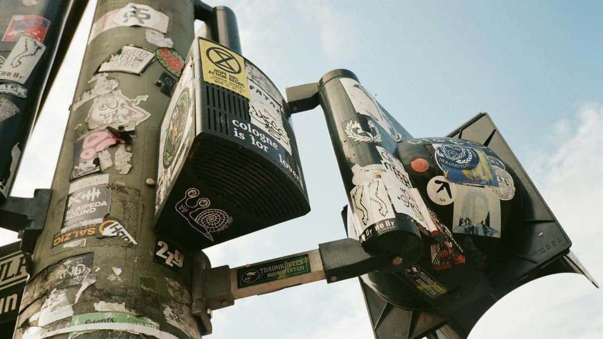 Low angle view of urban street light poles adorned with various colorful stickers against a blue sky.