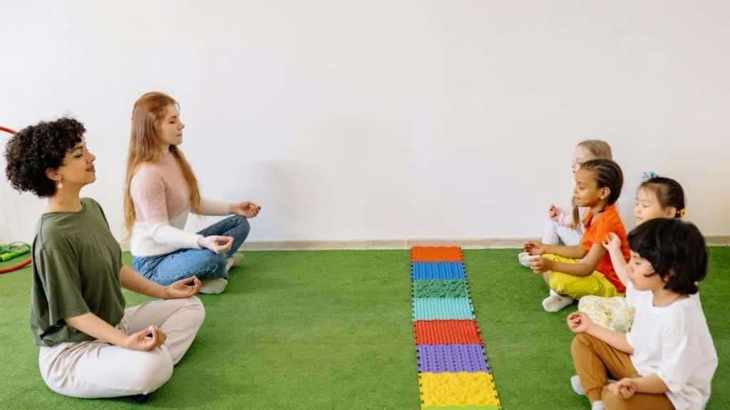 Kids and teachers in a preschool yoga session practicing mindfulness indoors.
