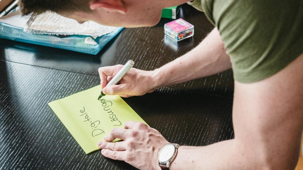 Man writes digital solutions on a note at a desk indoors, showcasing creativity.