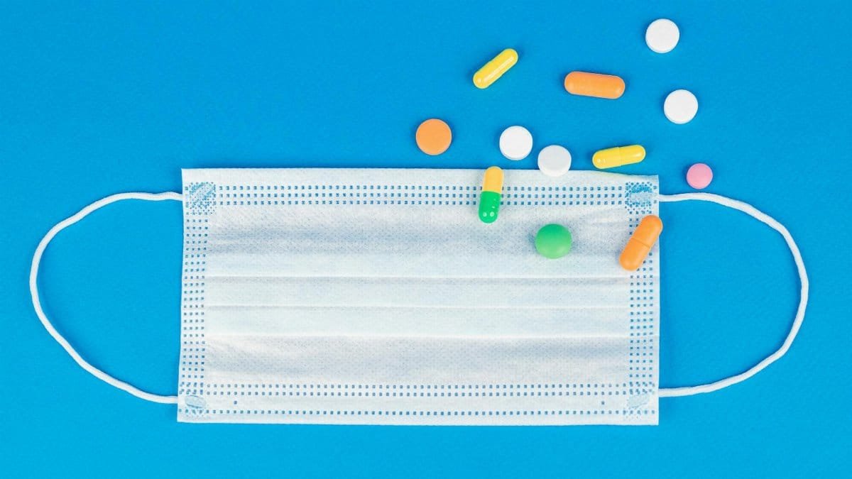 Face mask and various pills on blue background symbolizing healthcare and pandemic response.