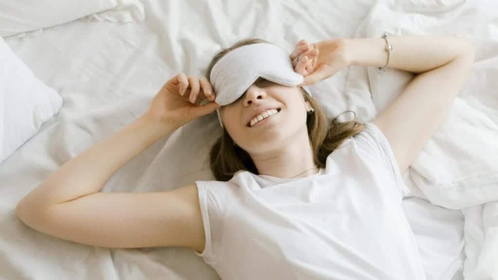 A serene young woman enjoying relaxation with a sleep mask in her cozy bed.