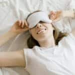 A serene young woman enjoying relaxation with a sleep mask in her cozy bed.