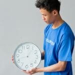 Male volunteer in a blue shirt holds a wall clock, showing the concept of time management.