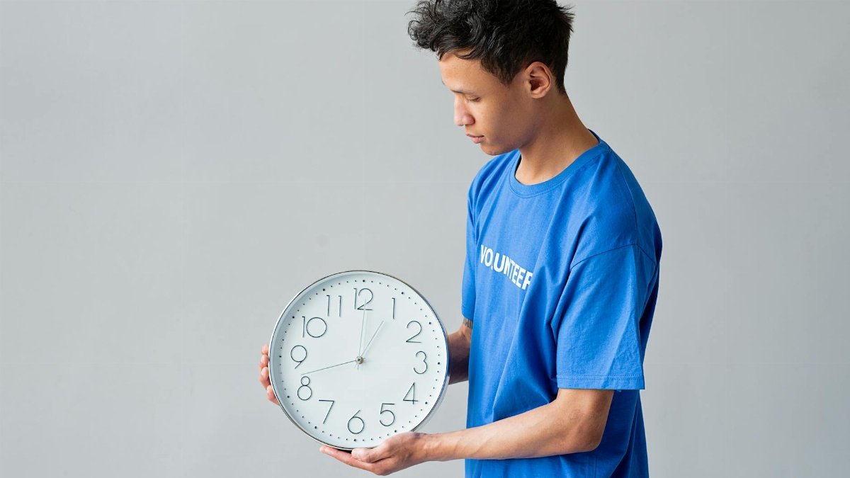 Male volunteer in a blue shirt holds a wall clock, showing the concept of time management.