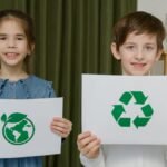 Two children holding eco-friendly signs indoors, promoting sustainability.