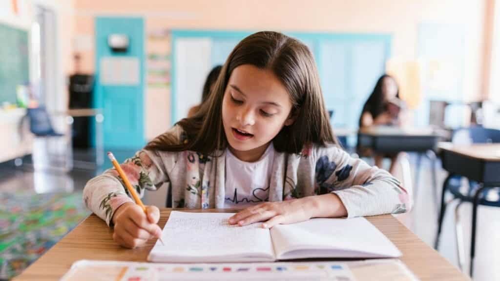 Focused young girl writing in her notebook in a classroom setting, showcasing learning and education.