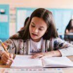 Focused young girl writing in her notebook in a classroom setting, showcasing learning and education.