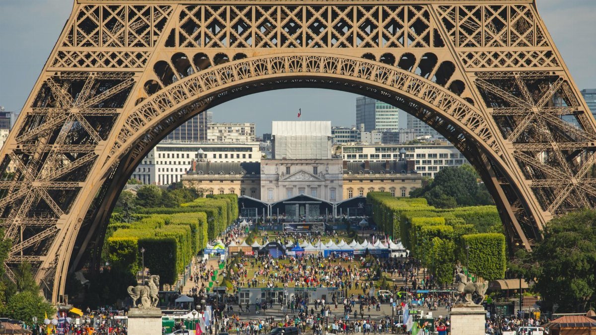 Vibrant scene under the Eiffel Tower in Paris with a bustling crowd and clear skies.