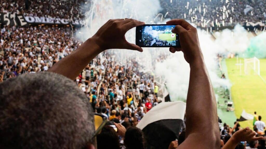 Thrilling football match scene with fans capturing the moment on a smartphone from the stadium stands.