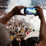 Thrilling football match scene with fans capturing the moment on a smartphone from the stadium stands.